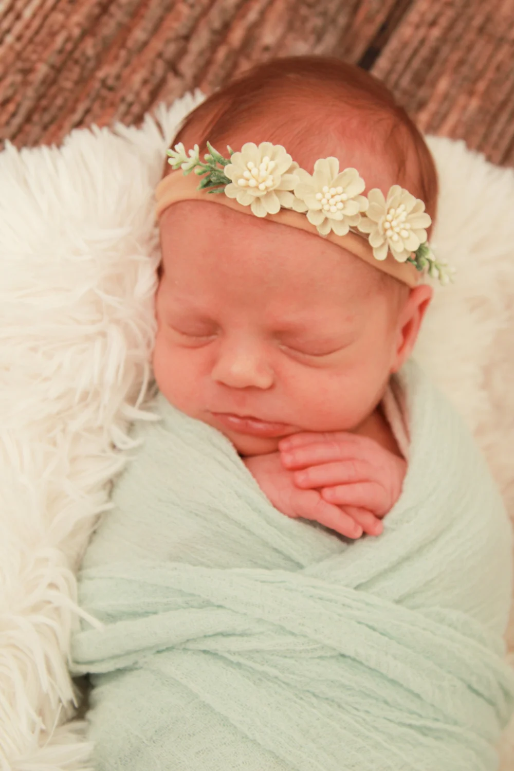Newborn baby girl swaddled in a mint green wrap with a floral headband during a Nassau County newborn photography session