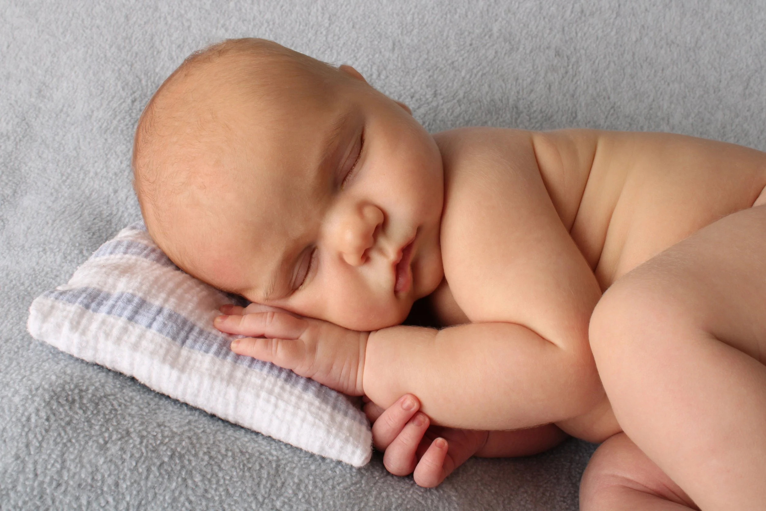 Close-up portrait of a sleeping newborn baby resting on a striped pillow during a family photography session